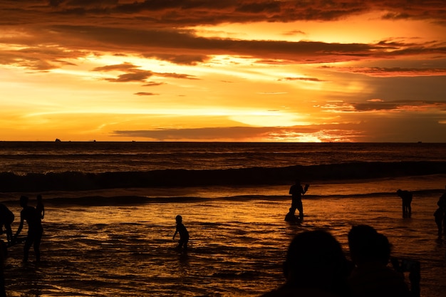 Personnes bénéficiant de la plage de la mer après le coucher du soleil sous le ciel doré