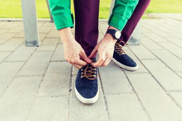 personnes, chaussures et concept de mode - gros plan sur des mains masculines attachant des lacets de chaussures dans la rue