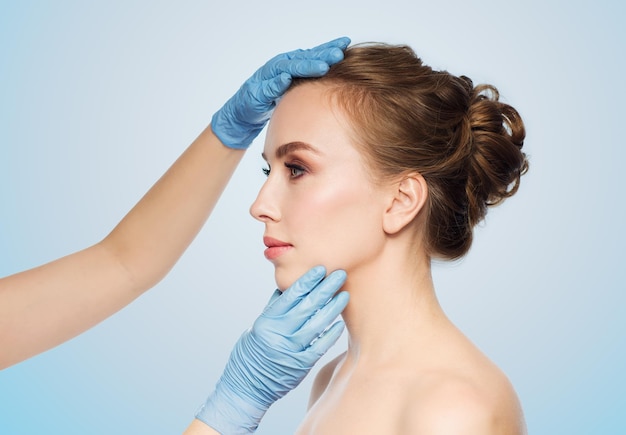 personnes, cosmétologie, chirurgie plastique et concept de beauté - mains de chirurgien ou d'esthéticienne touchant le visage d'une femme sur fond bleu