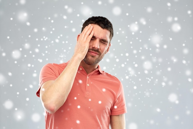 personnes, crise, hiver, noël et concept de stress - homme malheureux souffrant de maux de tête sur la neige sur fond gris