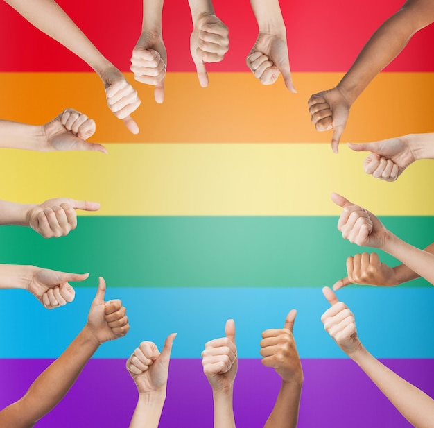 personnes, fierté gaie, geste et concept homosexuel - mains humaines montrant les pouces vers le haut en cercle sur fond de rayures de drapeau arc-en-ciel