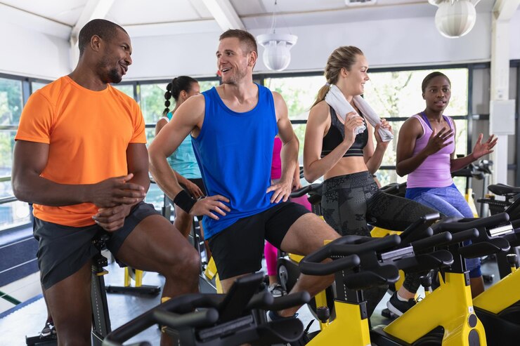 Photo des personnes en forme interagissant entre elles en faisant de l'exercice sur un vélo d'exercice dans un centre de remise en forme