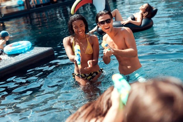 Personnes jouant avec des pistolets à eau colorés dans la piscine.