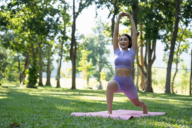 Personnes matures en bonne santé faisant du yoga au parc Femme asiatique faisant de l'exercice sur l'herbe verte avec un tapis de yoga