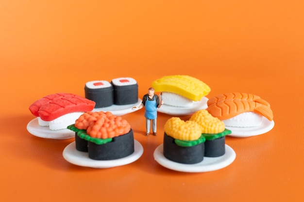 Personnes miniatures, chef faisant des sushis sur fond orange