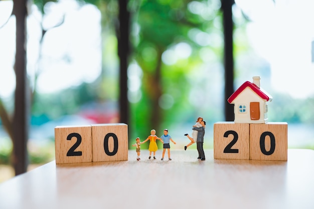 Photo personnes miniatures, famille heureuse debout avec mini maison et bloc de bois 2020 en utilisant comme concept de famille et de propriété