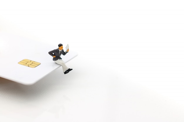 Personnes miniatures: homme d'affaires, lecture de livre sur carte de crédit.