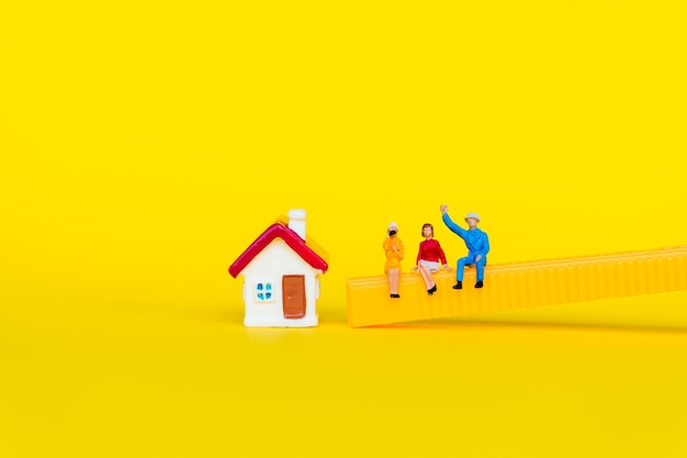 Personnes miniatures, homme et femme assis avec mini maison sur fond jaune en utilisant comme réunion d'affaires et concept social