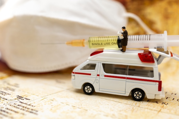 Des personnes miniatures se tiennent sur une ambulance avec un masque médical et une seringue de vaccin COVID-19. Vaccin et santé Concept médical.