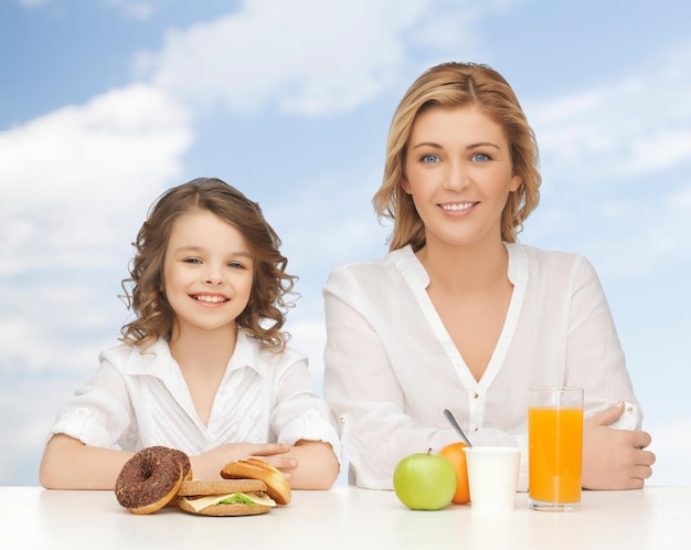 personnes, mode de vie sain, concept de famille et de nourriture - mère et fille heureuses mangeant un petit-déjeuner sain sur fond de ciel bleu