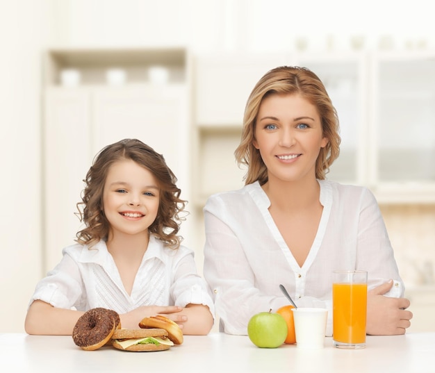 personnes, mode de vie sain, famille et concept d'aliments malsains - mère et fille heureuses mangeant des aliments différents sur fond de cuisine à domicile