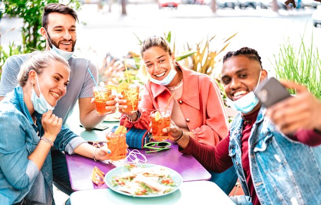 Personnes multiculturelles prenant selfie avec des masques ouverts au bar à cocktails