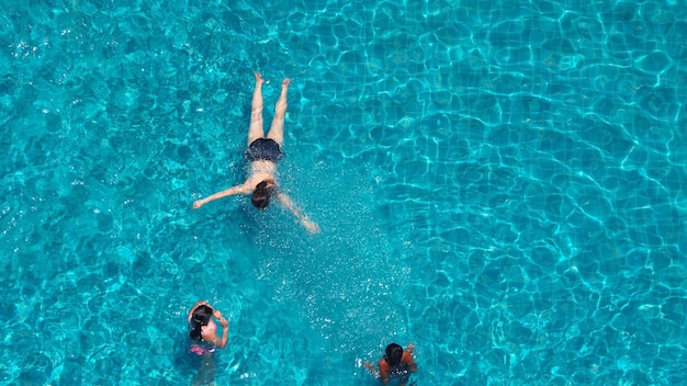 Les personnes nageant dans la piscine de l'hôtel qui ont de l'eau bleue et la lumière du soleil se reflètent dessus et l'angle de vue de dessus.