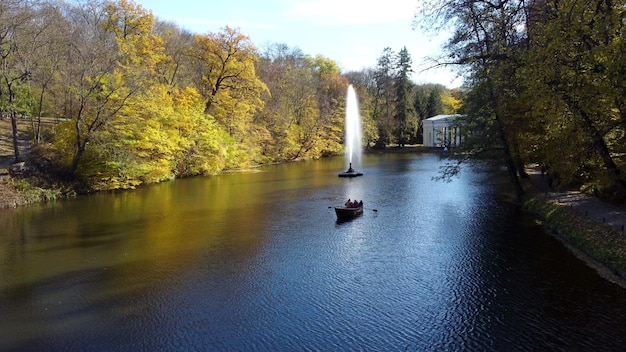 Personnes naviguant en bateau sur le lac fontaine décorative arbres feuilles jaunes dans le parc
