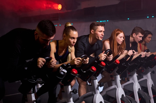 Les personnes prenant la perte de poids avec la machine aérobie pour un corps mince, assis sur un vélo, entraînement cardio intensif au gymnase de fitness