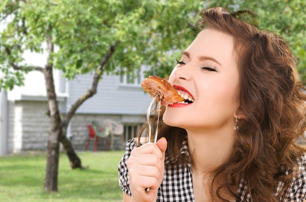 personnes, régime alimentaire et concept alimentaire - jeune femme affamée mangeant de la viande à la fourchette sur fond de maison et de jardin d'été