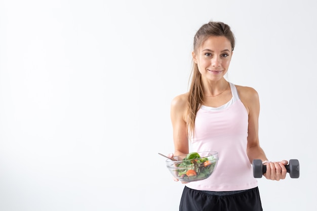 Personnes, régime alimentaire et concept de mode de vie sain - Portrait de femme avec salade et haltère sur fond blanc avec espace de copie.