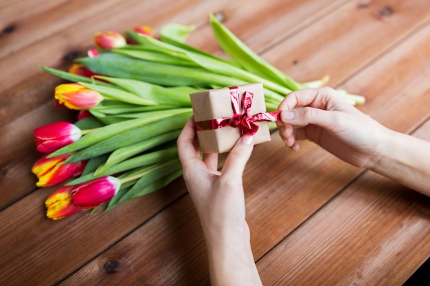 personnes, vacances et concept d'accueil - gros plan d'une femme tenant une boîte-cadeau et des fleurs de tulipes