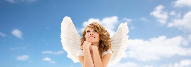Photo personnes, vacances, noël et concept religieux - heureuse jeune femme ou adolescente avec des ailes d'ange sur fond bleu ciel et nuages