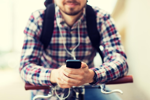 personnes, voyages, technologie, loisirs et mode de vie - gros plan sur un jeune homme hipster dans des écouteurs avec smartphone et vélo à pignon fixe écoutant de la musique dans la rue de la ville