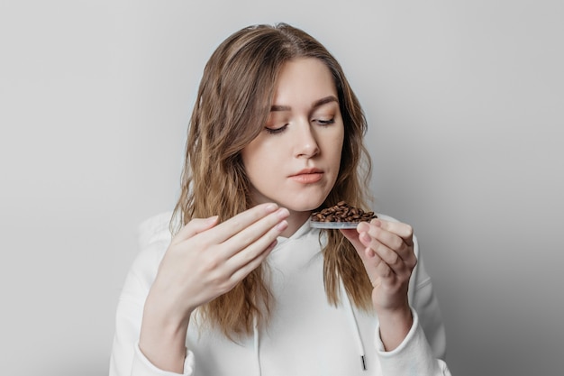 Perte d'odeur Portrait en gros plan d'une jeune femme caucasienne reniflant des grains de café isolés