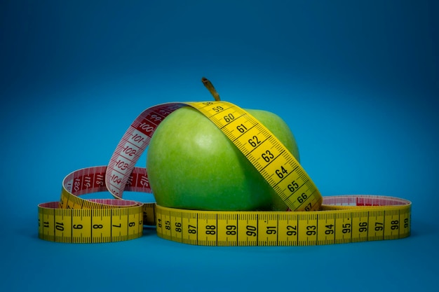 Perte de poids et concept d'alimentation saine avec un ruban à mesurer et une pomme verte sur fond bleu