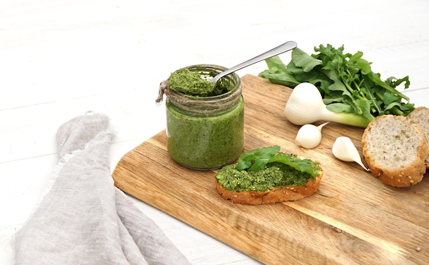 Pesto de roquette dans un bocal et feuilles de roquette honnête et toast se trouvent côte à côte