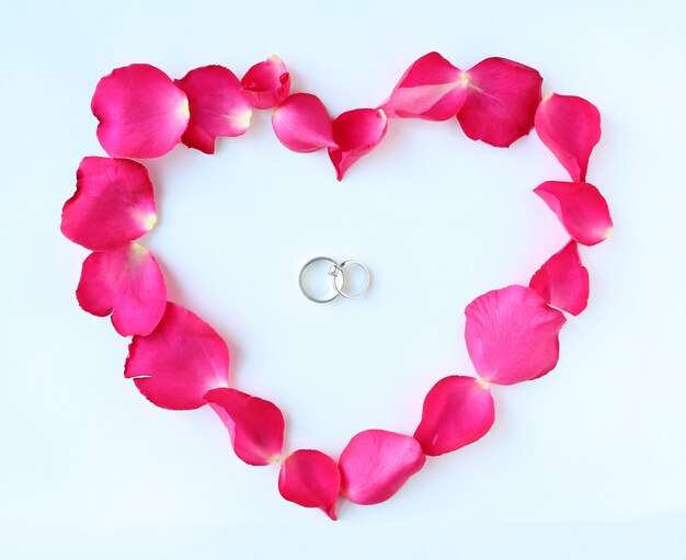 Photo pétales de fleur rose en forme de coeur avec alliances isolés sur fond blanc.