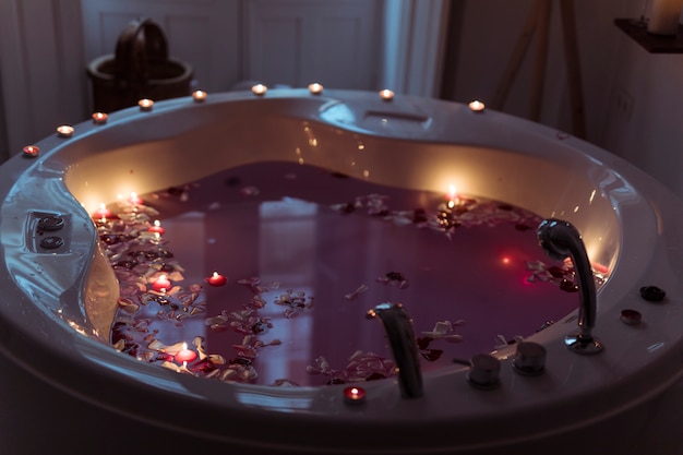 Pétales de fleurs dans un spa avec de l'eau et des bougies allumées sur les bords