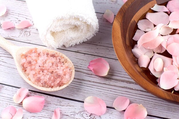 Pétales de rose sur un bol en bois avec du sel rose et une serviette blanche sur fond de bois