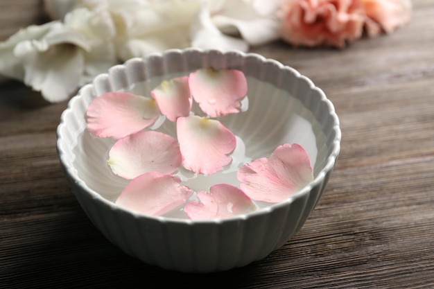 Pétales de rose rose tendre dans un bol d'eau sur fond de bois