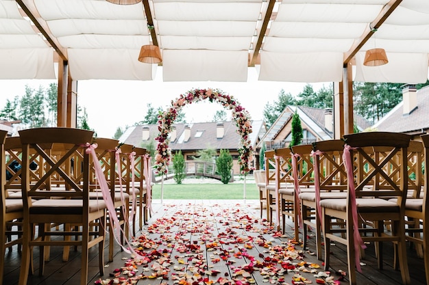 Pétales de roses éparpillés sur la route décor de mariage Chaises en bois dans la zone de banquet de l'arrière-cour L'arche pour la cérémonie de mariage est décorée de fleurs et de verdure