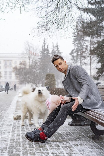 Petit ami avec un bouquet d'hortensias de fleurs roses attendant sa petite amie et marchant et jouant avec un chien. à l'extérieur pendant que la neige tombe. Concept de la Saint-Valentin, demande en mariage. mangues