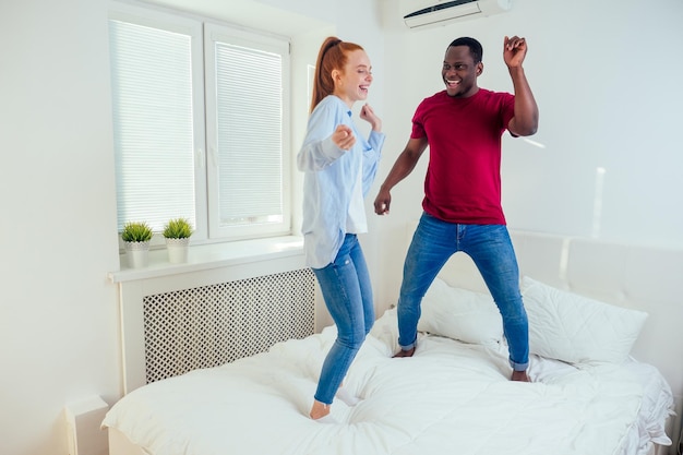 Petit ami hispanique latino et petite amie rousse aux cheveux roux sautant sur le lit le matin. Déménagement dans une maison à louer.