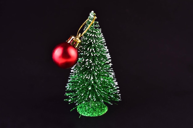 Petit arbre de Noël avec une boule rouge sur un fond en bois noir.