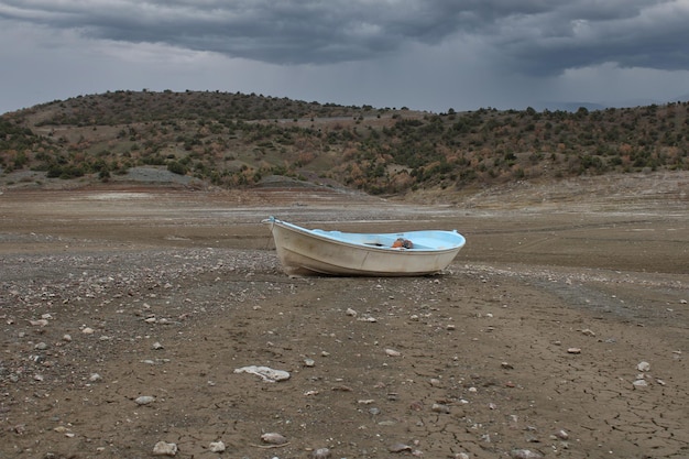 Petit bateau blanc qui est resté au-dessus du sol alors que le lac s'assèche C'est le temps de la sécheresse