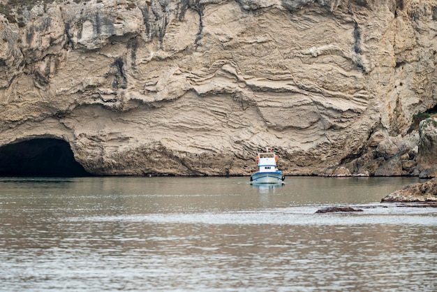 Petit bateau de pêche naviguant entre les récifs et avec un grand fond de falaises