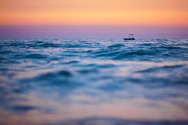 Petit bateau sur les vagues au coucher du soleil, focus sur le bateau, premier plan flou, espace pour copie