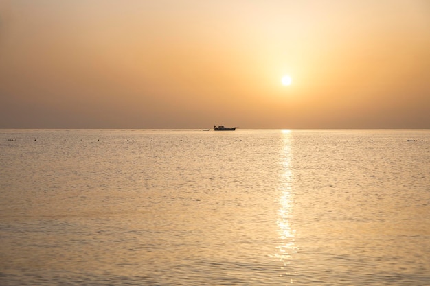 Petit bateau avec voile et disque orange du coucher de soleil sur la mer pendant le coucher du soleil sur la mer Méditerranée Turquie Province d'Antalya