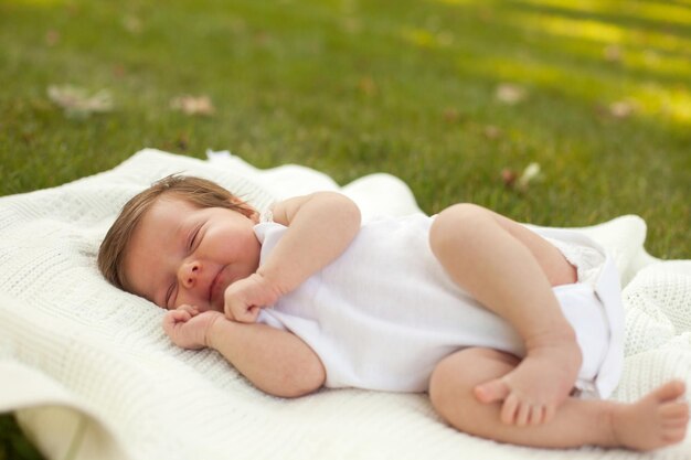 Petit beau bébé en vêtements blancs dormant sur la couverture blanche sur l'herbe