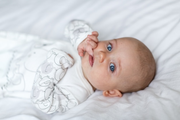 Un petit bébé allongé sur le lit sur un drap blanc et regardant