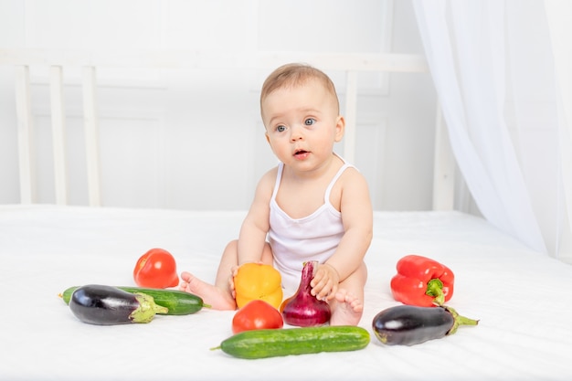 Petit bébé assis sur le lit dans la pépinière avec des légumes, concept de nourriture pour bébé,