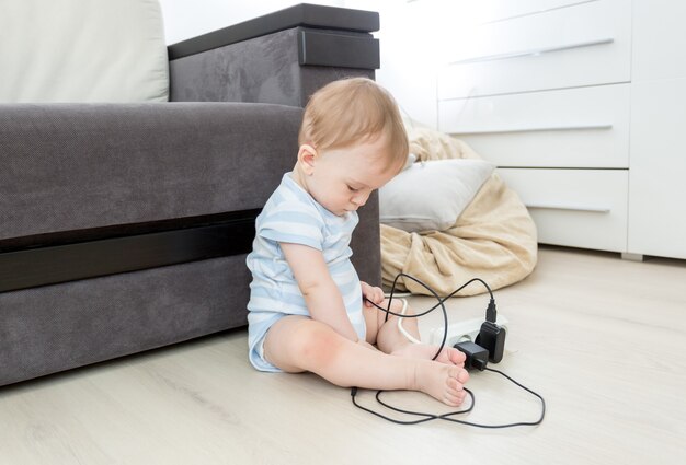 Petit bébé assis seul dans le salon et jouant avec des câbles électriques