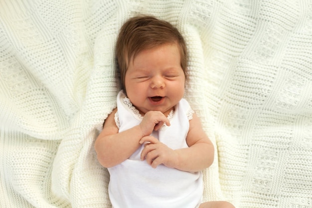 Petit bébé charmant en vêtements blancs couché et en lacet sur la couverture blanche