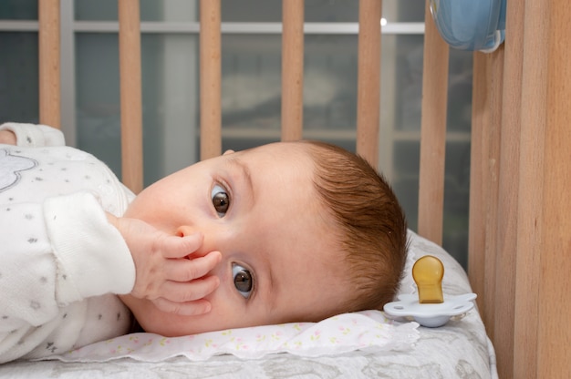 Petit bébé couché sur un berceau en train de sucer un doigt dans la bouche.