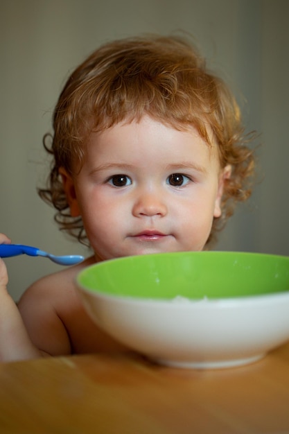 Petit bébé drôle dans la cuisine mangeant avec les doigts de la plaque