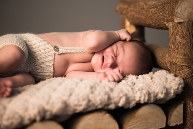 Petit bébé endormi nouveau-né se trouve sur la peau sur un tabouret en bois sur fond gris