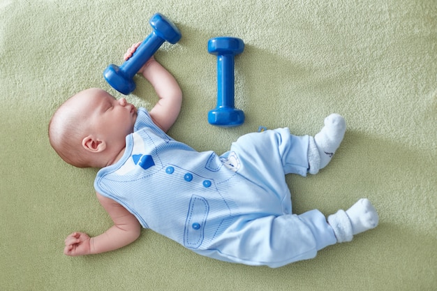 Petit bébé est allongé avec des haltères dans ses mains