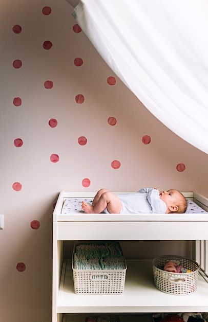 Petit bébé est allongé sur la table des enfants près de la fenêtre. Il y a un nouveau-né sur la table à langer. Photo verticale