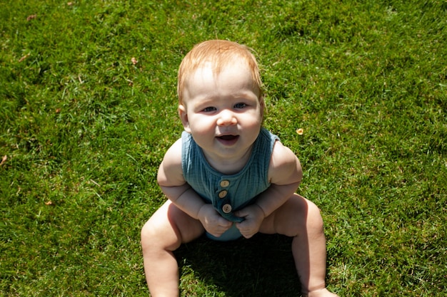 Petit bébé est assis sur l'herbe dans le parc et souritÉté et soleil éclatantPromenade en plein air